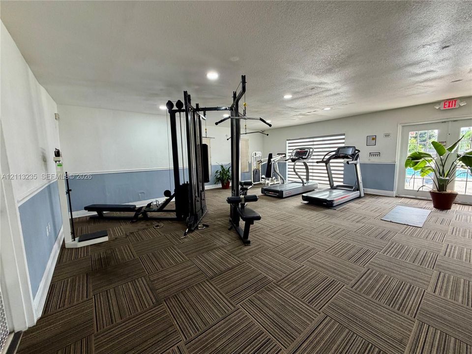 Fitness space featuring patterned carpet tiles, recessed ceiling lighting, chair rail molding, and a double-glass door
