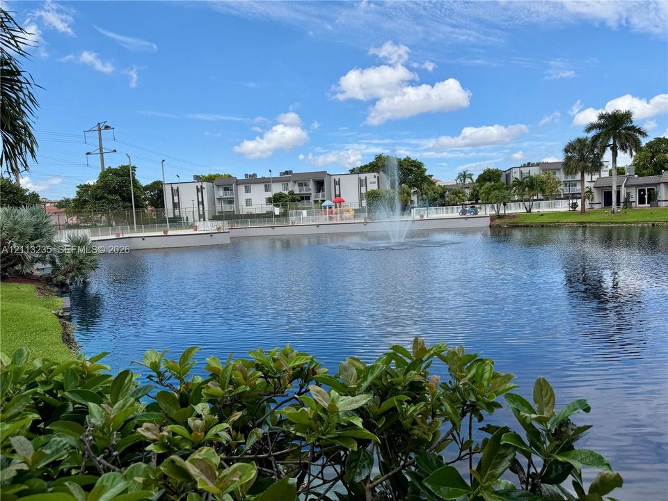 Waterfront setting featuring a central fountain, manicured landscaping, and perimeter fencing