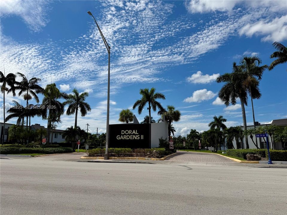 Entrance to Doral Gardens II featuring professional landscaping, mature palm trees, and decorative hardscaping