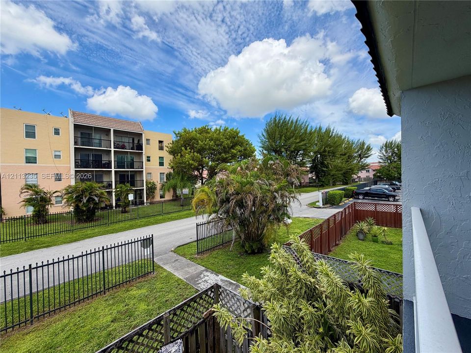 Exterior balcony featuring metal railings, privacy lattice fencing, and a concrete pathway