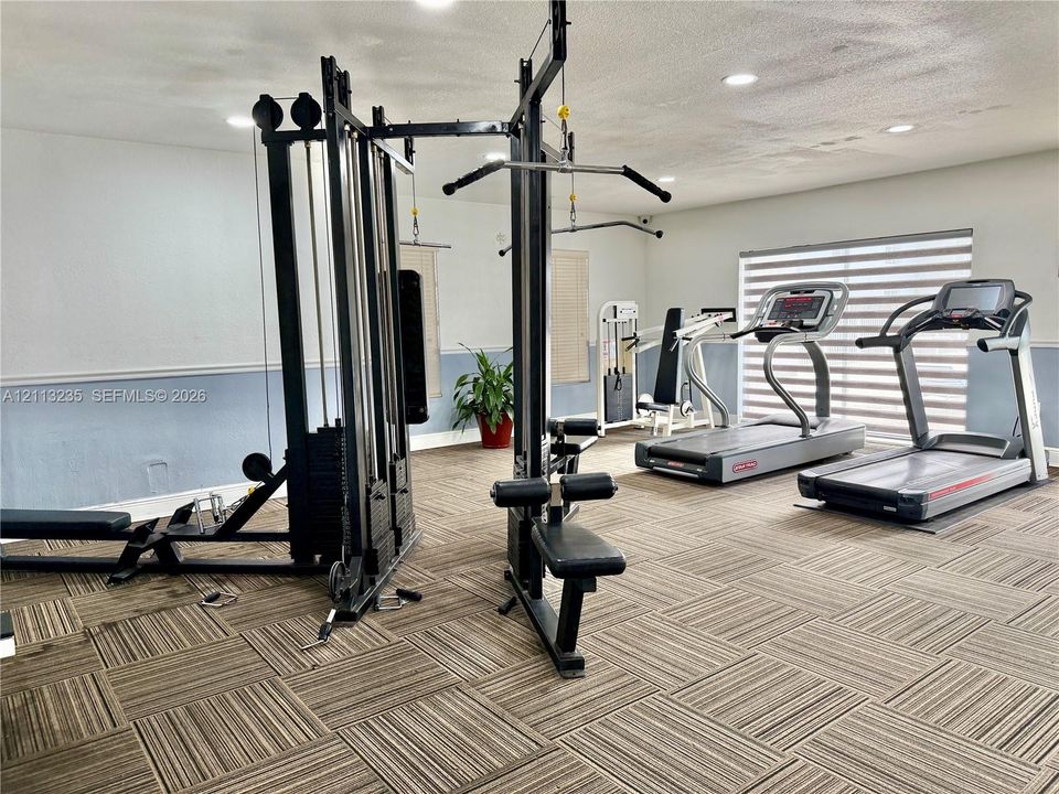 Fitness space featuring recessed lighting, patterned modular floor tiles, and horizontal window shades
