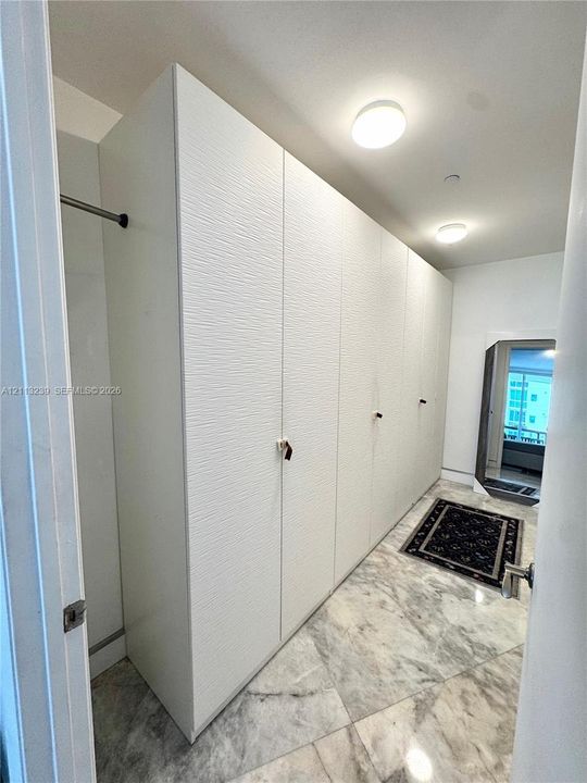 Full-height white built-in cabinetry with textured fronts, stone-finish flooring, and recessed ceiling lighting
