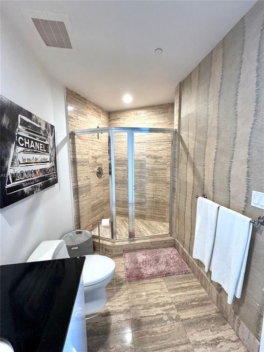 Bathroom featuring a corner glass-enclosed shower, stone tile flooring, stone-tiled shower walls, wall-mounted metallic towel bar, and textured wall treatment