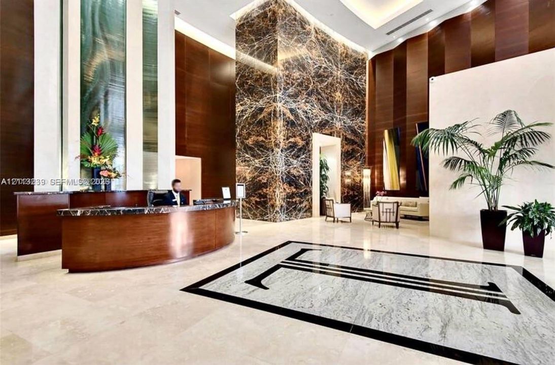 Grand lobby entrance featuring high-contrast stone flooring, a prominent full-height natural stone feature pillar, recessed cove lighting, and curved wood-veneer reception desk