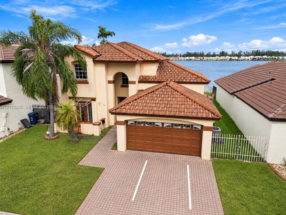 Two-story exterior featuring a clay tile roof, stucco finish, paved driveway, integrated two-car garage, and waterfront location