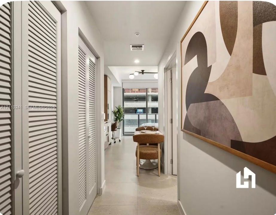 Hallway featuring dual white louvered closet doors, neutral large-format tile flooring, and a modern multi-bulb ceiling fixture
