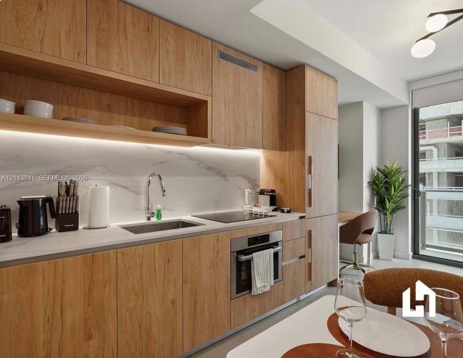 Custom wood-finish cabinetry, stone-surface backsplash, integrated stainless steel appliances, recessed under-cabinet lighting, and built-in flat-panel cabinetry