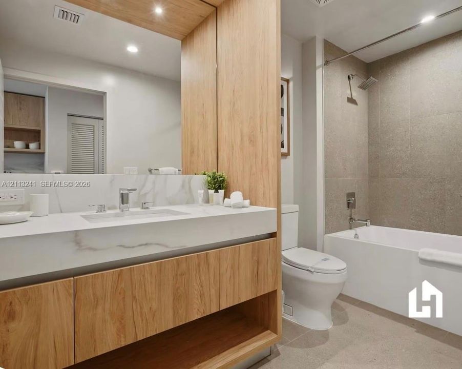 Floating wood-finish vanity with an integrated basin, stone-composite countertop, full-width mirror, textured tile shower surround, and recessed lighting