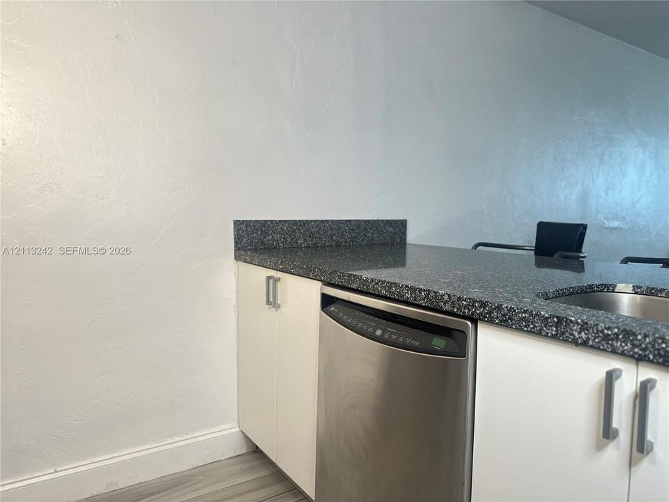 Kitchen featuring a solid-surface countertop, stainless steel dishwasher, undermount sink, and flat-panel cabinetry with metal hardware