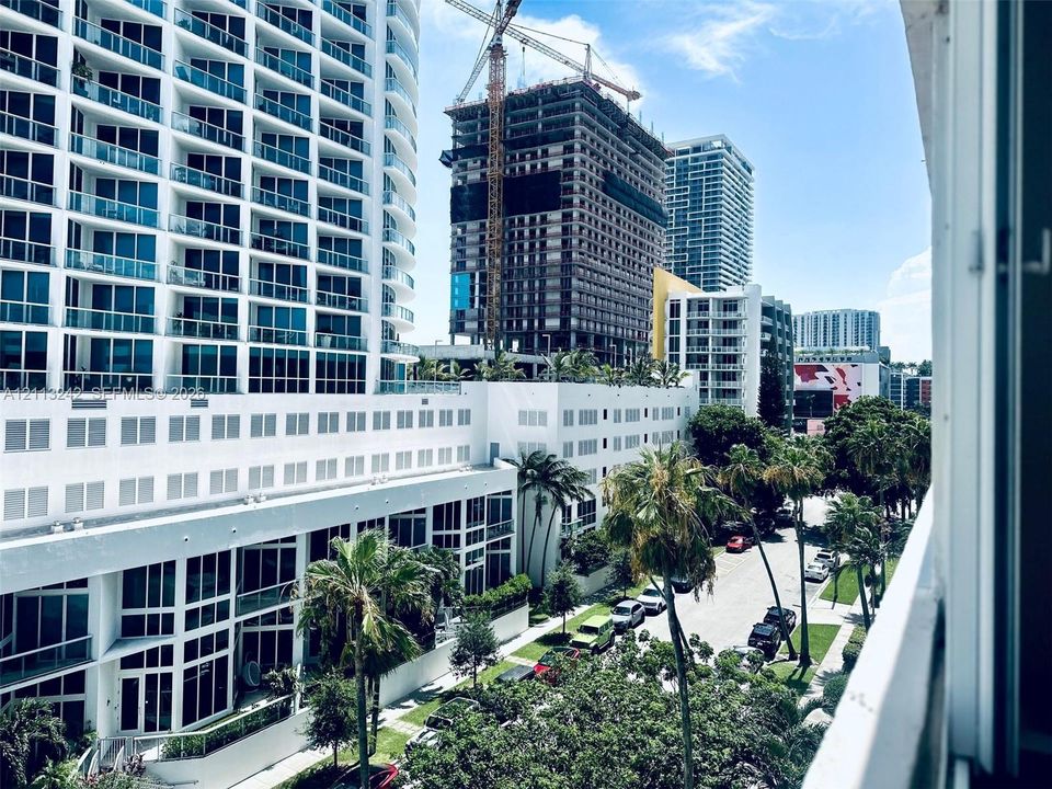 Urban high-rise exterior featuring floor-to-ceiling glass windows, exterior balcony railings, and manicured palm tree landscaping