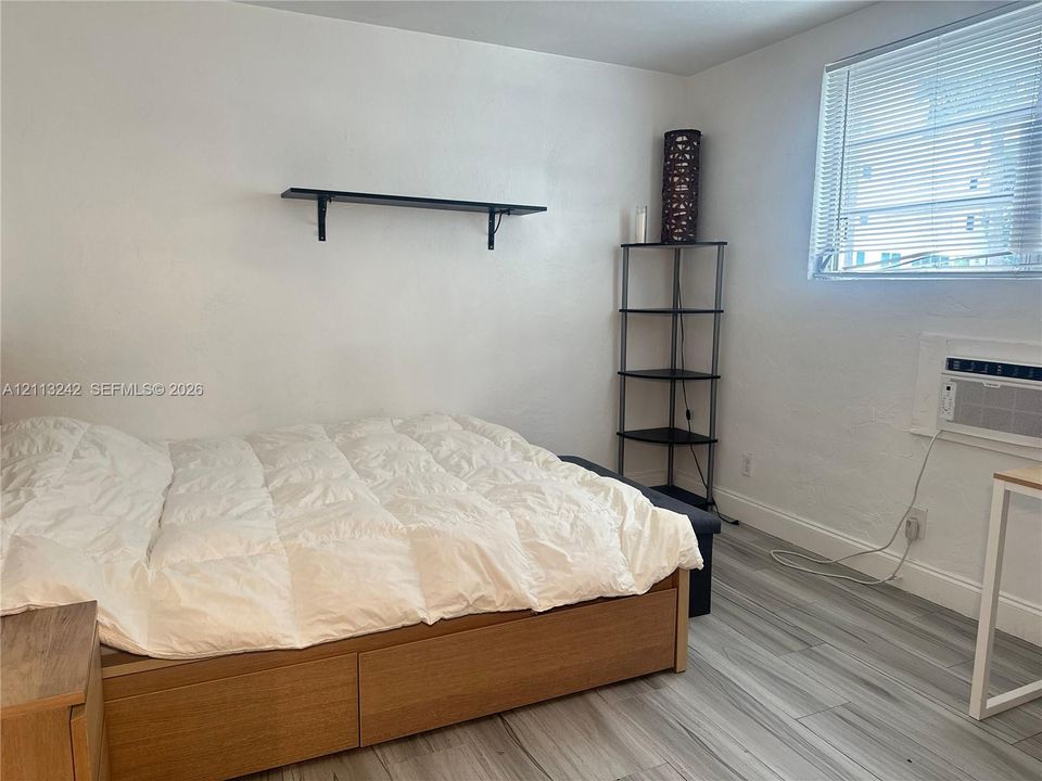 Interior space featuring wood-finish flooring, a wall-mounted floating shelf, and a built-in wall-mounted air conditioning unit