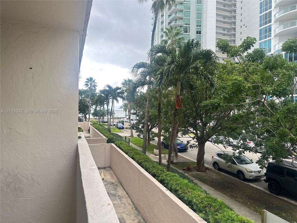 Outdoor balcony featuring stucco partition walls and concrete flooring, overlooking mature palm trees and landscaped greenery