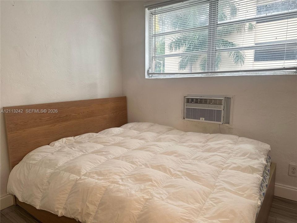 Room featuring a wide window with horizontal blinds, built-in through-wall air conditioning unit, and wood-finish flooring