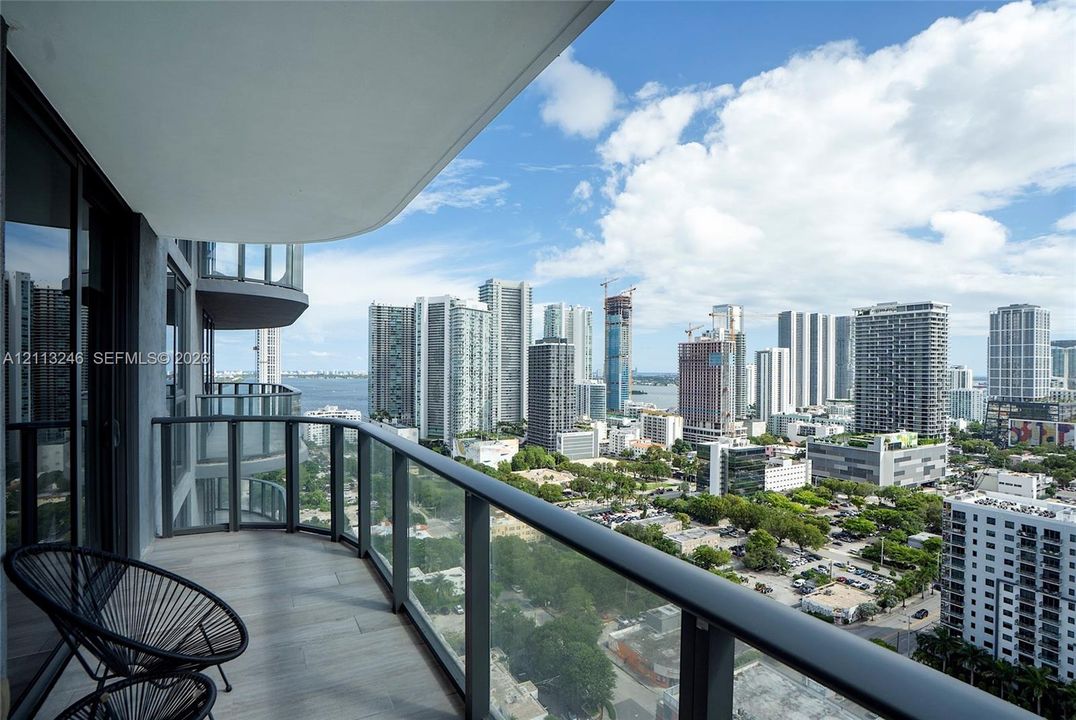 Private balcony featuring wood-finish flooring, glass panel railings, and expansive urban skyline scenery