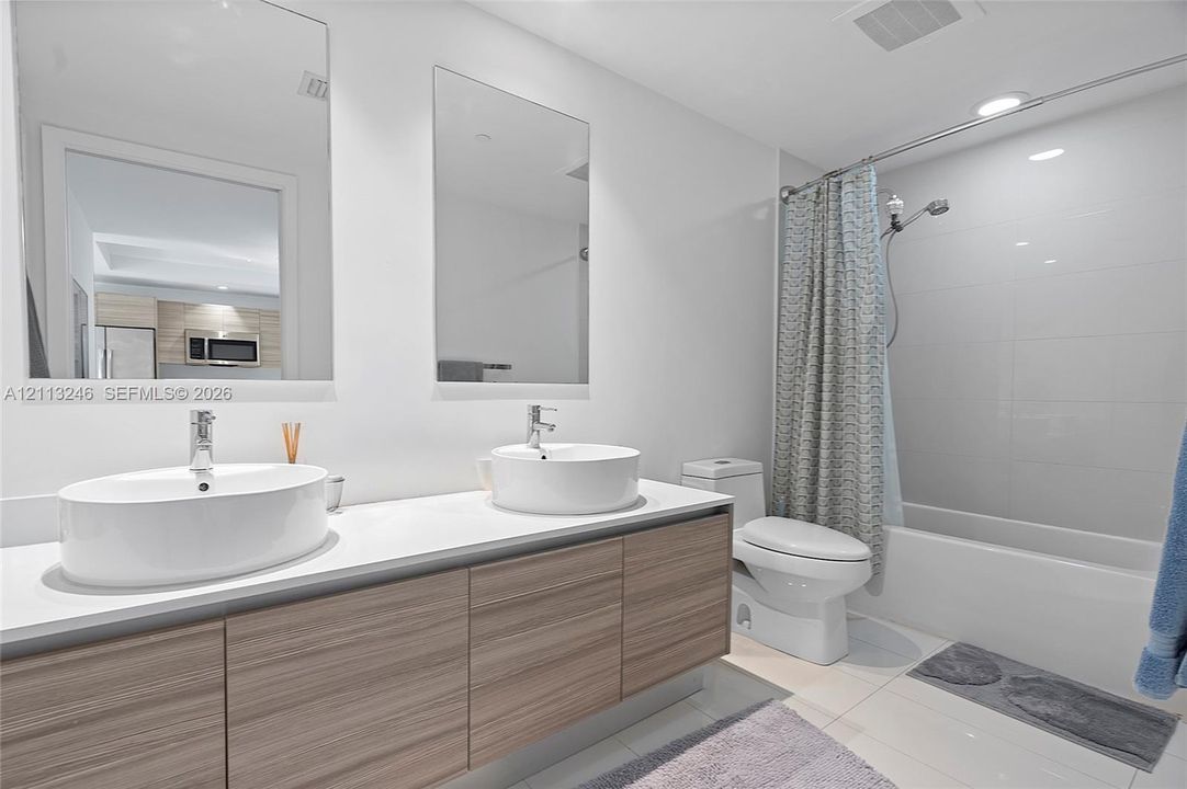Floating wood-finish vanity with dual vessel sinks, white countertop, and frameless rectangular mirrors, accompanied by a combined soaking tub and shower with tile surround