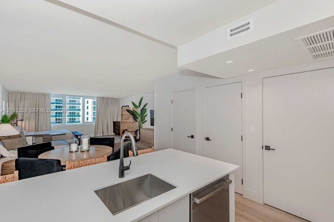 Kitchen island featuring a solid-surface countertop, stainless steel undermount sink, and matte black faucet, complemented by wood-finish flooring and recessed ceiling lighting