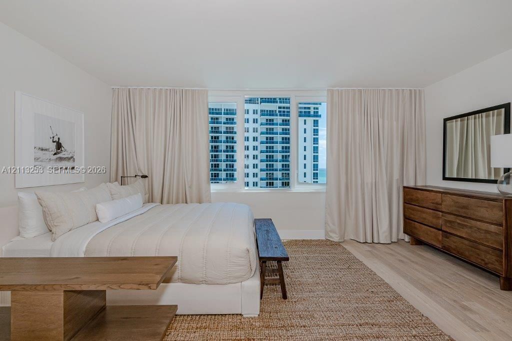 Floor-to-ceiling windows with neutral drapery and light-tone wood-finish flooring