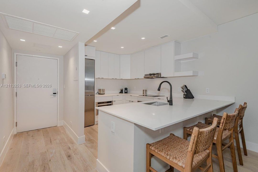 Kitchen featuring flat-panel cabinetry, light-toned countertops, a matte black high-arch faucet, integrated stainless steel appliances, and wood-finish flooring