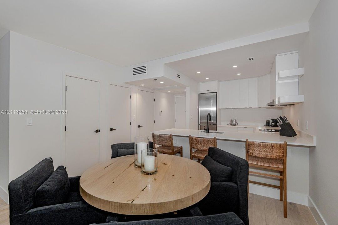 Kitchen featuring white cabinetry, solid-surface countertops, integrated stainless steel appliances, matte black plumbing fixtures, and wood-finish flooring