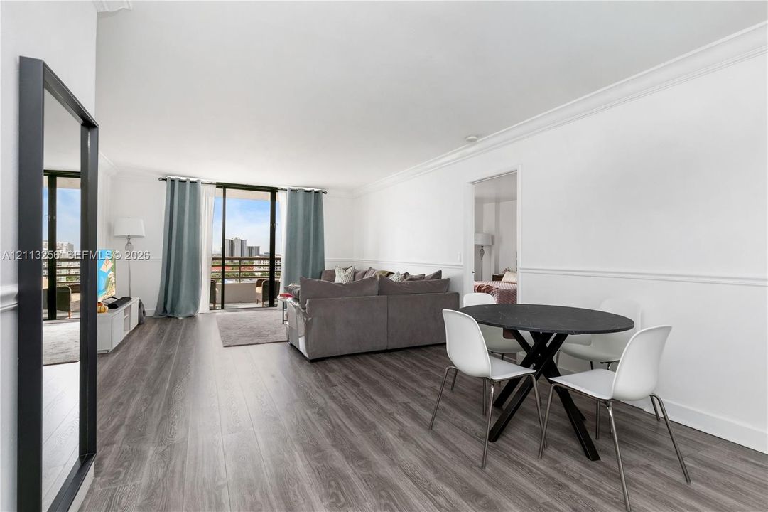 Open-concept living space featuring wood-finish flooring, crown molding, chair rail trim, and glass sliding doors providing exterior balcony access