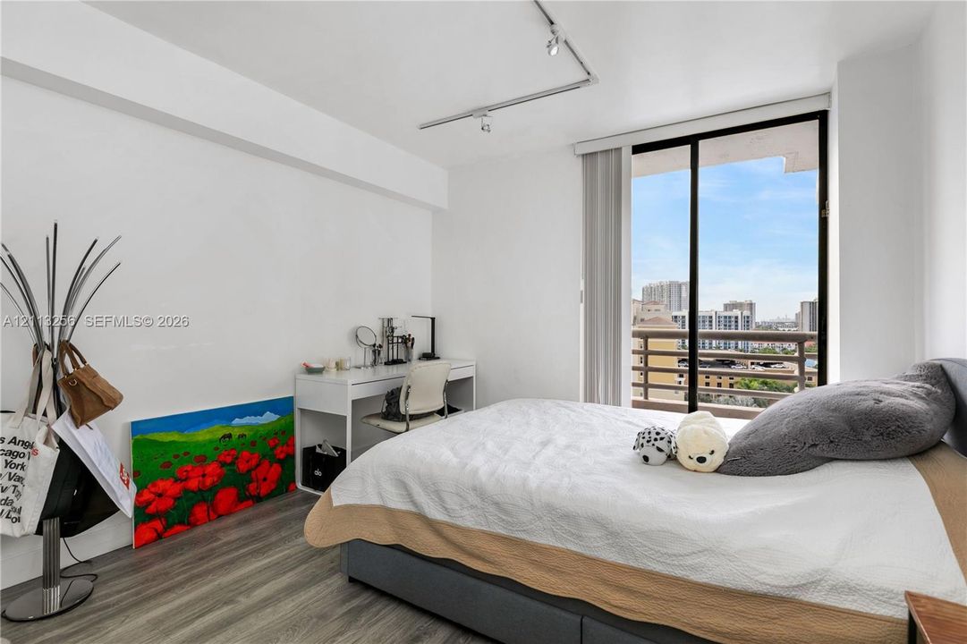 Sliding glass door opening to a private balcony, wood-finish flooring, and ceiling-mounted track lighting