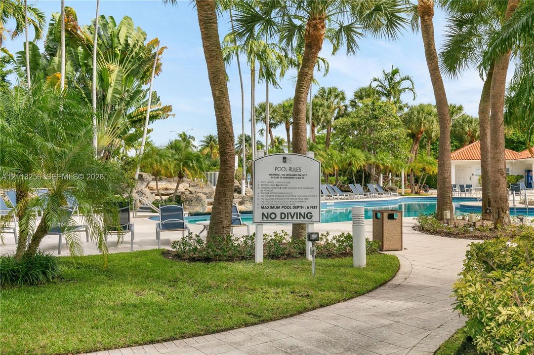 Swimming pool featuring a rock waterfall, surrounded by concrete paver decking, professional landscaping, and palm trees