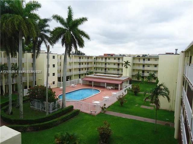 Outdoor swimming pool with surrounding deck, mature palm trees, manicured lawns, and multi-story exterior balconies