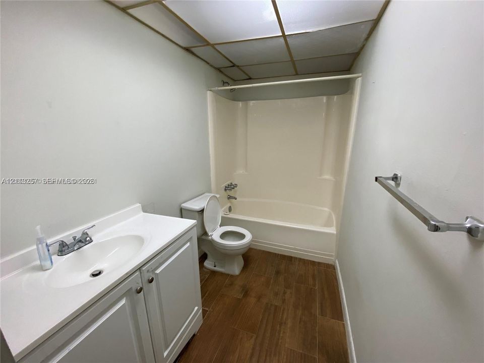 Bathroom featuring wood-finish flooring, white vanity cabinet with a integrated sink, and a combination tub and shower enclosure with wall-mounted plumbing fixtures