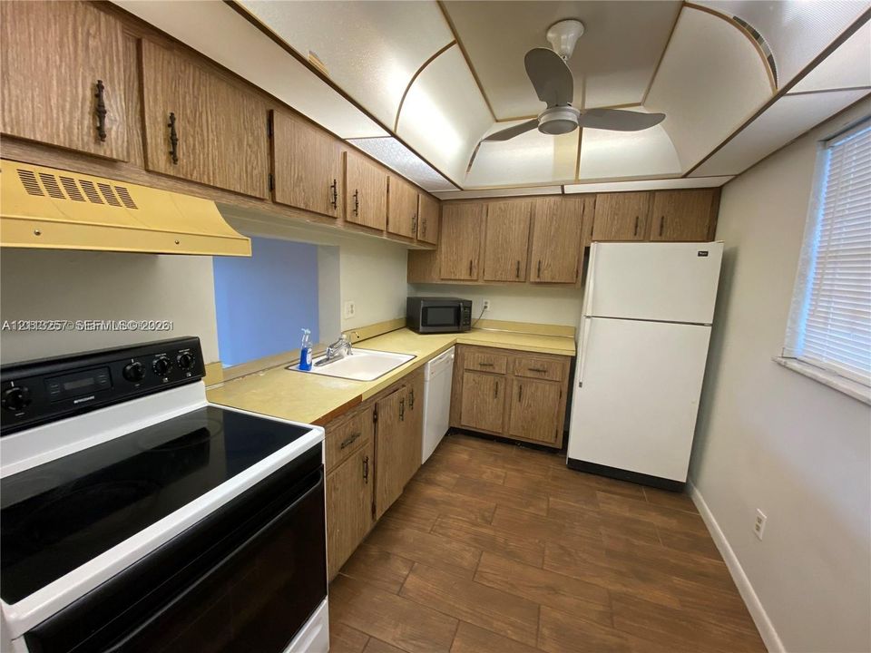 Kitchen featuring wood cabinetry, solid-surface countertops, wood-finish flooring, recessed ceiling lighting, and a ceiling fan