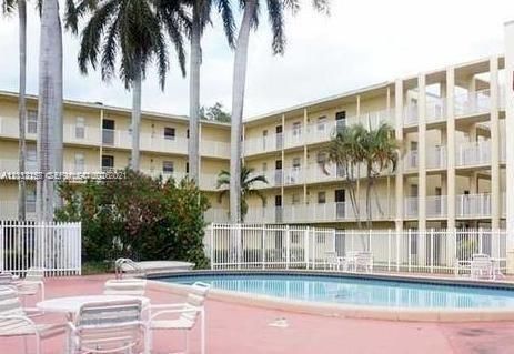 Multi-story residential building with private balconies and a fenced-in swimming pool area featuring mature palm trees