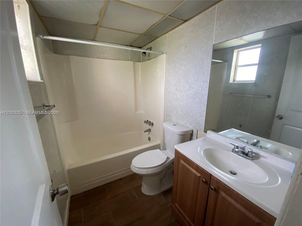 Bathroom featuring a composite tub and shower surround, wood-finish vanity with an integrated basin, wood-finish flooring, and a wall-mounted mirror