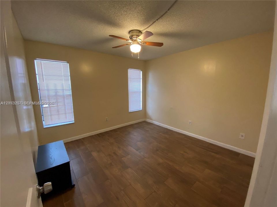 Room interior featuring wood-finish tile flooring, two windows with integrated blinds, and a central ceiling fan with integrated lighting