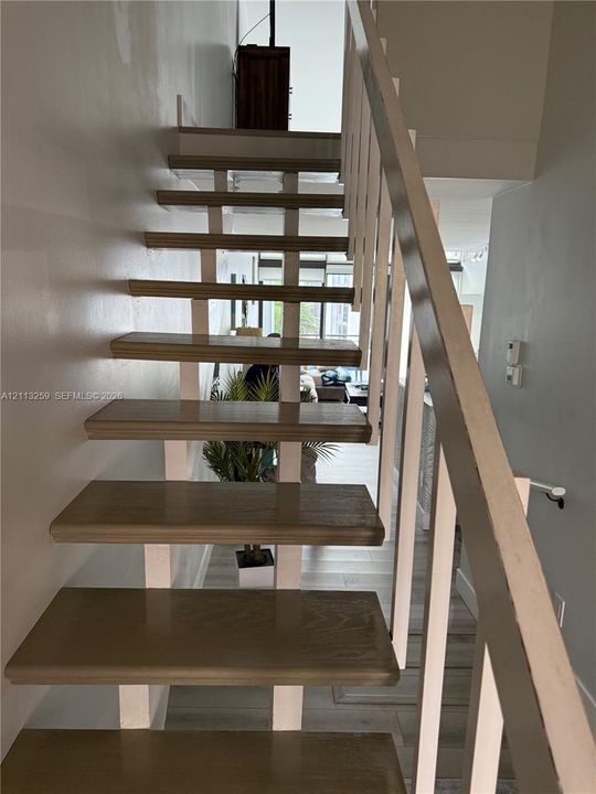 Open-riser staircase featuring wood-finish treads and a minimalist white metal railing