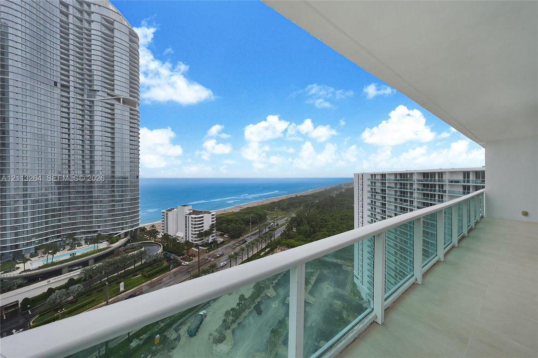 Covered balcony featuring tile flooring and a glass-paneled railing overlooking the coastline and ocean
