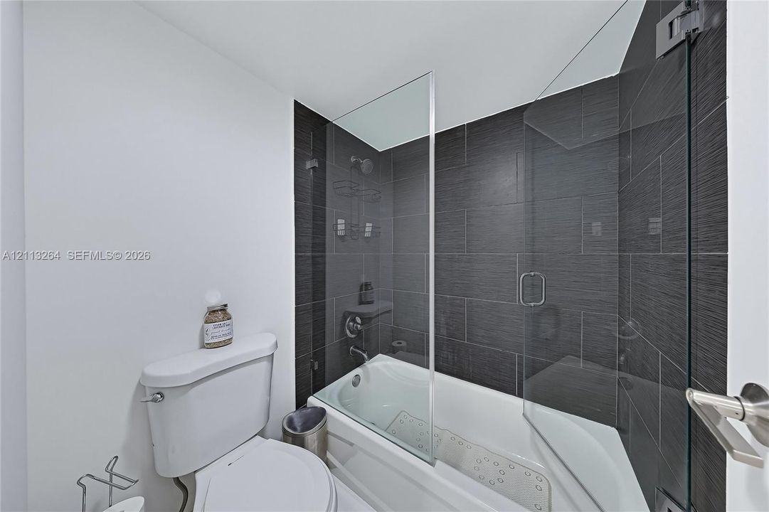 Bathtub featuring a glass shower panel, textured dark wall tiling, and chrome fixtures