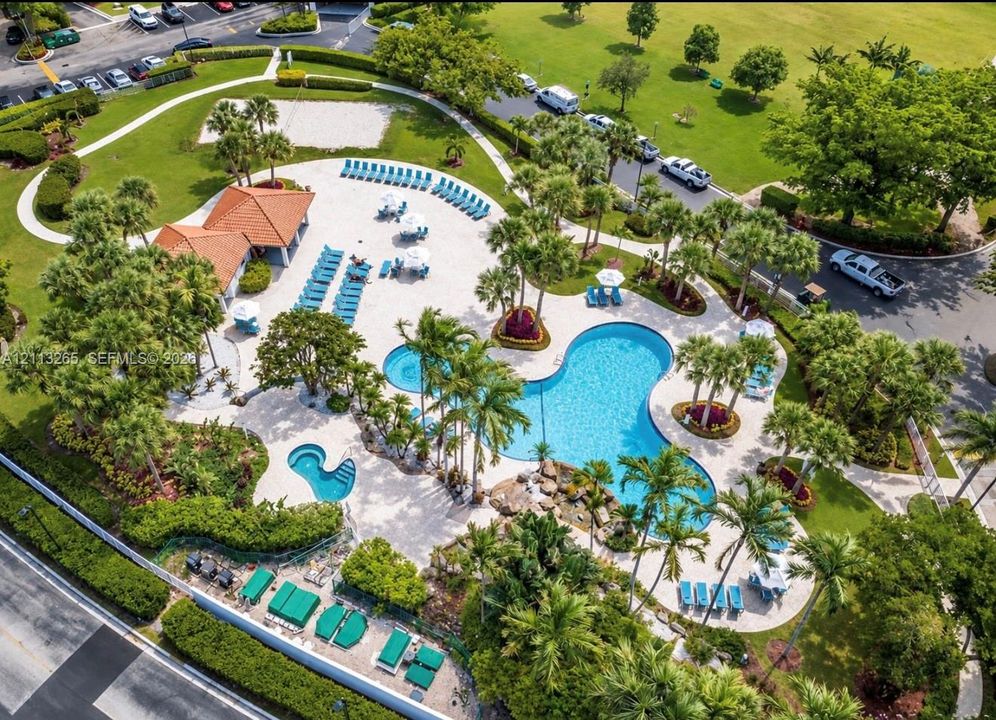 Community pool area featuring a large swimming pool, separate spa, tile-roofed pavilion, stone-accented water feature, and extensive hardscaping