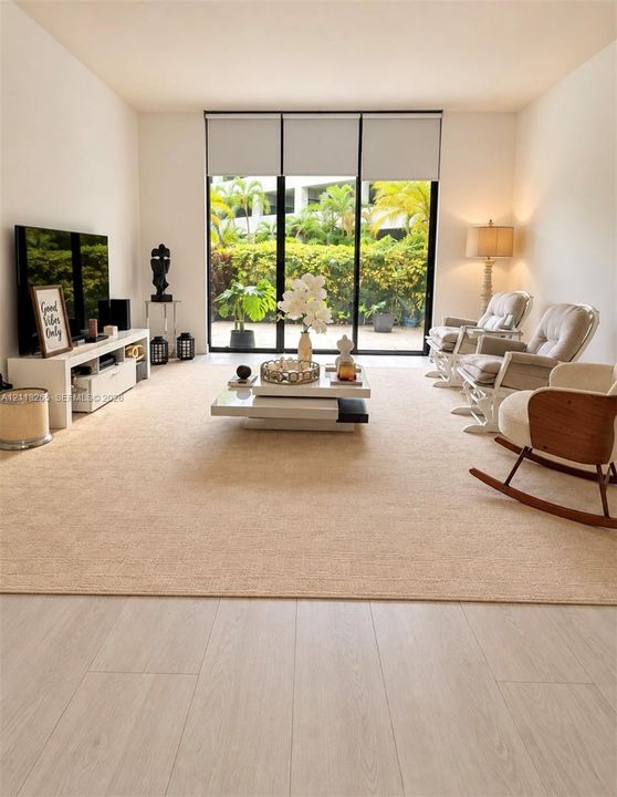 Living area featuring wood-finish flooring, floor-to-ceiling black-framed glass sliding doors, and neutral wall tones