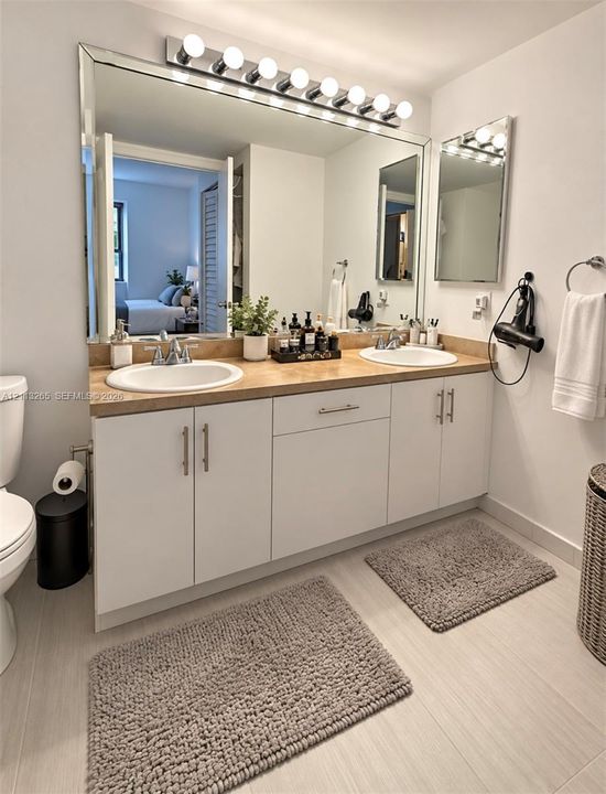 Dual-basin vanity featuring white cabinetry, a neutral countertop, undermount sinks, and a large plate-glass mirror with a multi-bulb light fixture