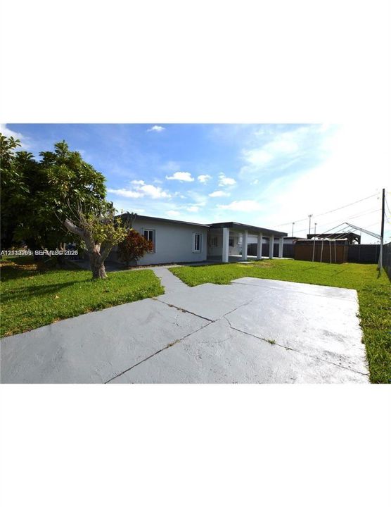 Exterior grounds featuring a paved concrete patio, a covered porch with structural support columns, and expansive lawn space