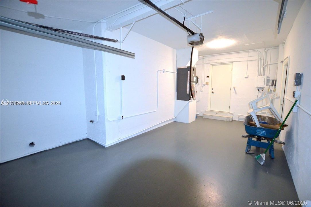 Garage space featuring painted concrete flooring, white walls, overhead door track system, and an exterior access door