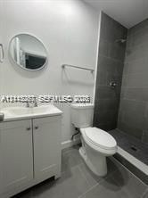 Bathroom featuring a white vanity cabinet with an integrated sink, oval wall-mounted mirror, floor-to-ceiling gray tile shower surround, and gray tile flooring