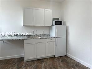 Kitchenette featuring white cabinetry, stone-surface countertops, an integrated sink with a gooseneck faucet, and wood-finish flooring