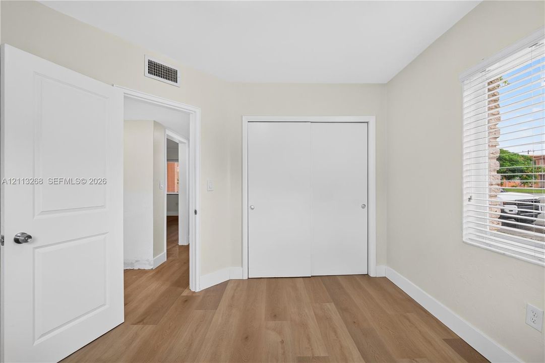 Interior space featuring wood-finish flooring, neutral wall paint, white interior doors, sliding closet doors, and horizontal window blinds