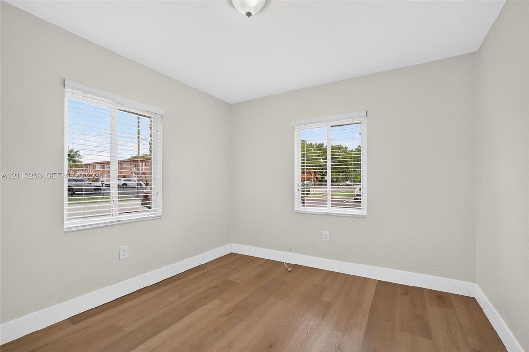 Neutral-toned interior room featuring wood-finish flooring, dual windows with horizontal blinds, and a ceiling-mounted light fixture