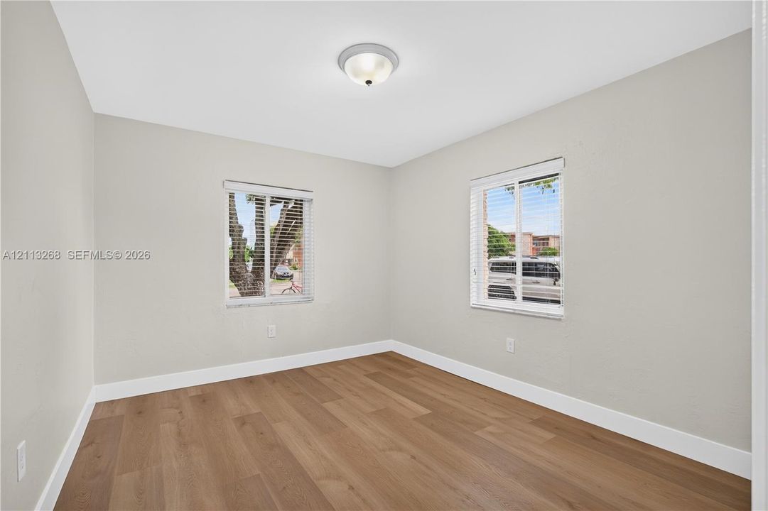 Room featuring wood-finish flooring, dual windows with horizontal blinds, neutral wall paint, and a ceiling-mounted light fixture