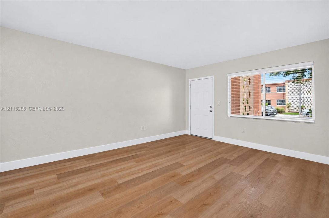 Neutral-toned interior space featuring wood-finish flooring, a white paneled entry door, and a horizontal window with adjustable blinds
