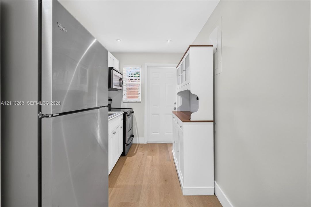Stainless steel refrigerator, wood-finish flooring, white shaker-style cabinetry, built-in hutch, and recessed lighting