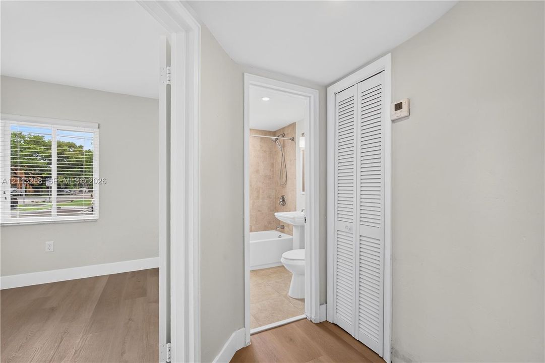 Hallway featuring wood-finish flooring, a white bifold closet door, and access to a bathroom equipped with a pedestal sink, tub-shower combination, and tiled wall surround