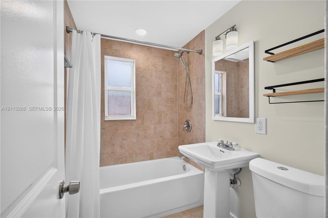 Full bathroom featuring a pedestal sink, framed mirror, wall-mounted light fixture, and a tub-shower combination with floor-to-ceiling tile surround