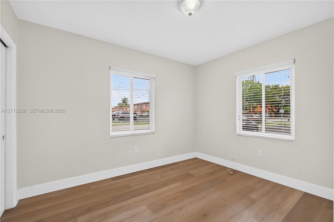 Neutral interior room featuring wood-finish flooring, two dual-pane windows with horizontal blinds, and a flush-mount ceiling light fixture